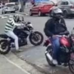 João, que estava vestindo uma blusa listrada branco e verde, estaciona a moto, uma Kawasaki 650 cilindradas, cinza chumbo. Ele se aproxima de outro homem, que está parado em outra moto. Em seguida, abre a mochila para pegar algo, e nesse momento dois indivíduos param de moto do outro lado da rua, e anunciam o assalto. (Foto: reprodução vídeo)