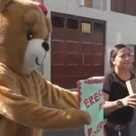 Um agente disfarçado de urso laranja, segurando uma placa (Foto: X)