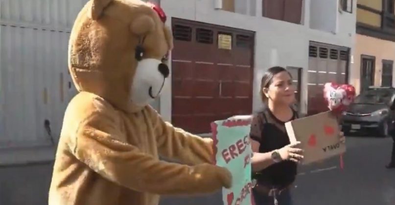 Um agente disfarçado de urso laranja, segurando uma placa (Foto: X)