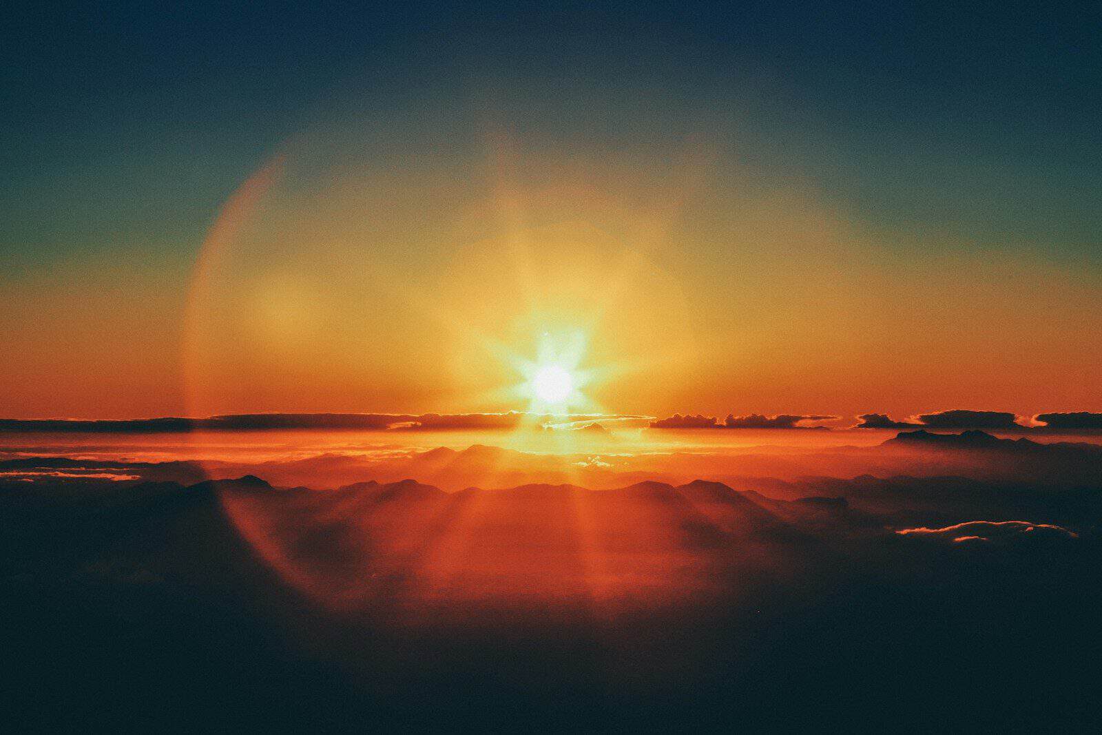 Low sun with a bright lens flare above a dark mountain range