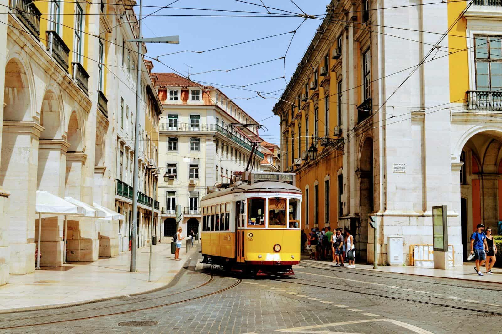 A yellow tram traveling through a street lined with historic buildings in Lisbon, Portugal.