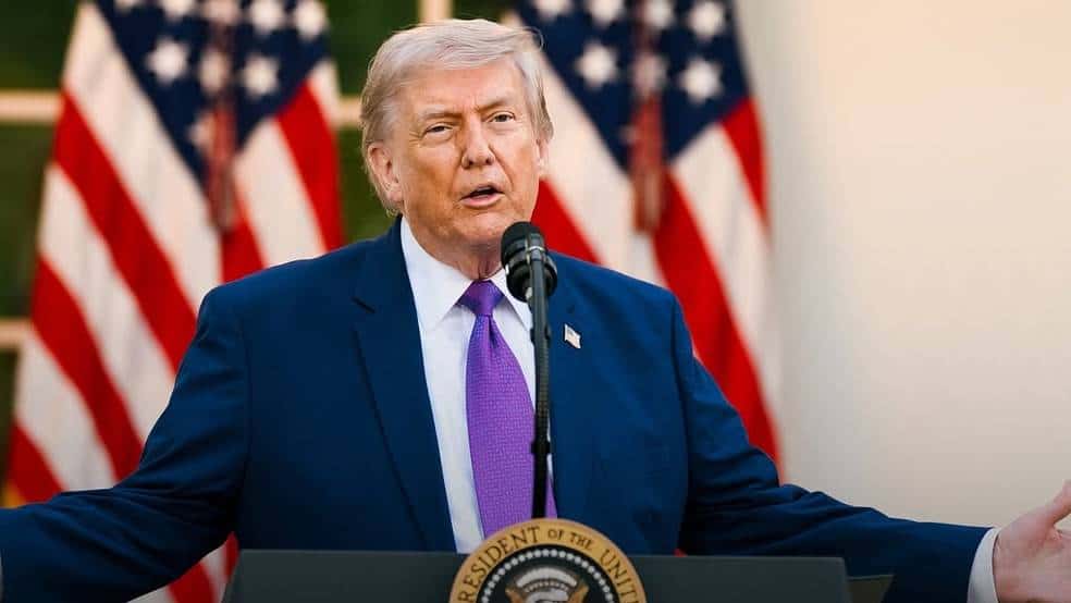 Donald Trump falando em evento com bandeiras dos EUA ao fundo.