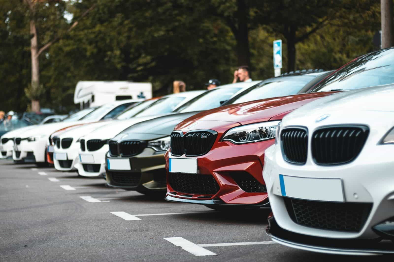 A row of parked cars including white, olive, and red sedans in a lot