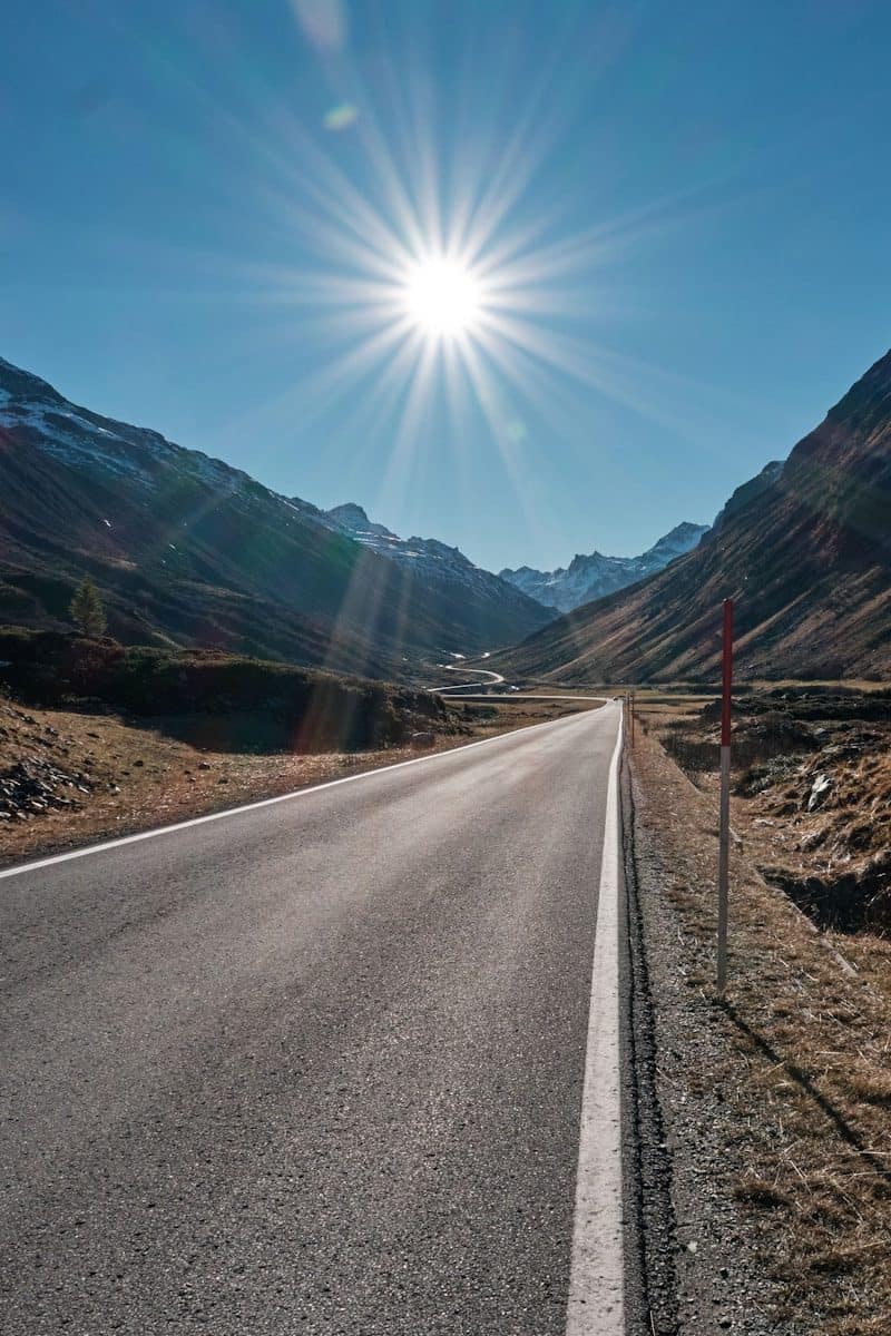 gray concrete road between brown mountains under blue sky during daytime