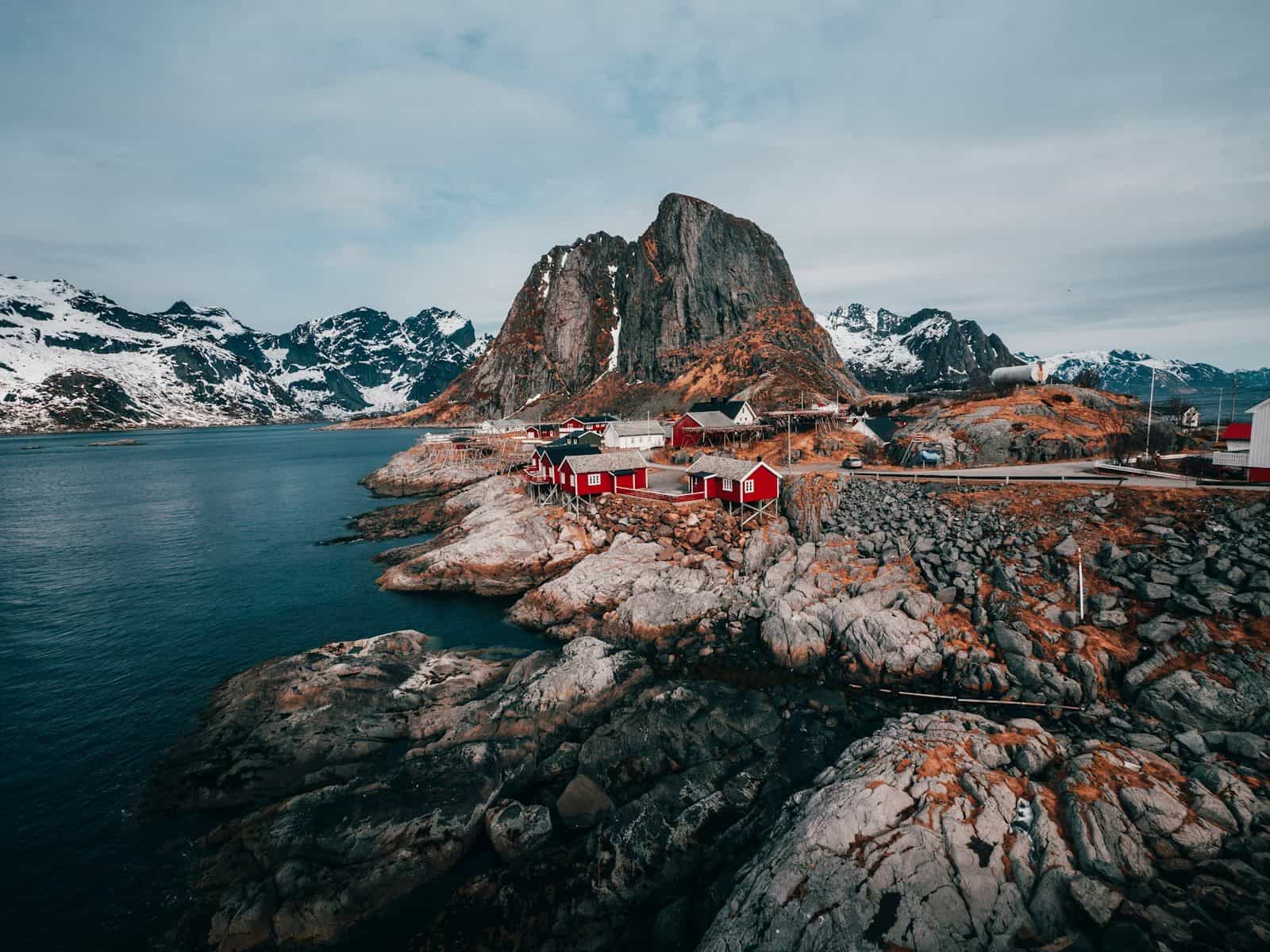 Red cabins on a rocky coastline beneath snow-capped mountains in Lofoten, Norway