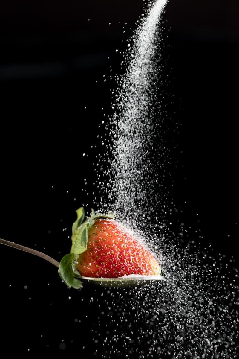 Sugar being poured onto a strawberry on a spoon