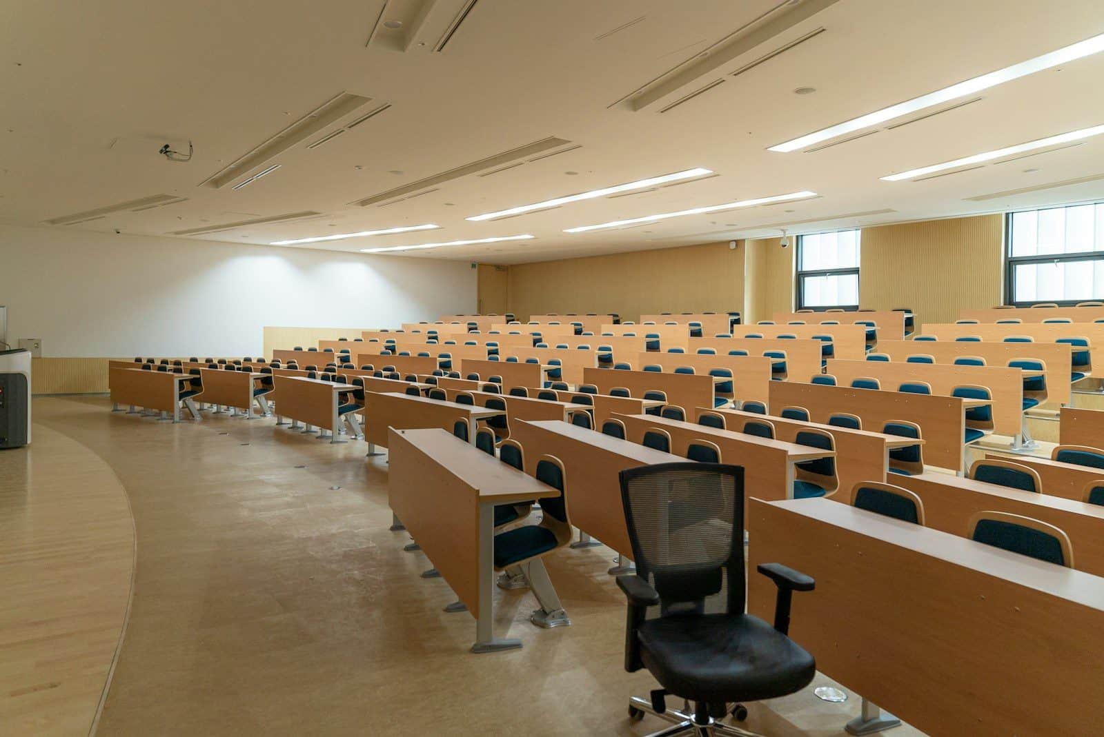 Rows of wooden desks and chairs in a large empty university lecture hall
