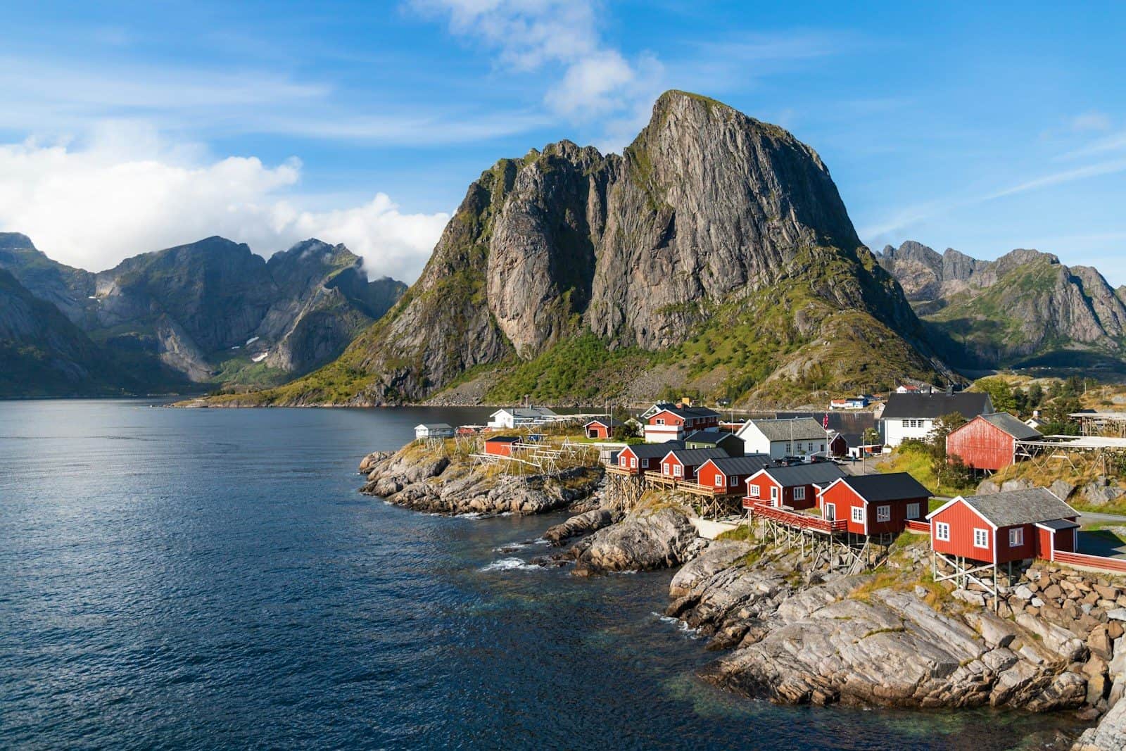 a group of houses by a body of water with mountains in the background with Lofoten in the background