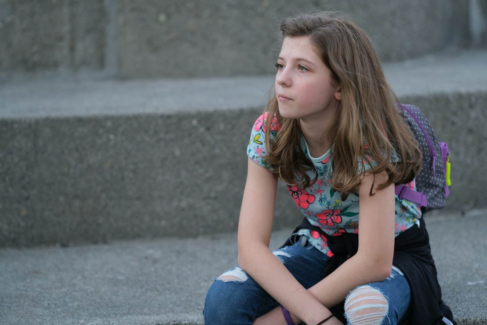 A young girl sitting on steps with a backpack on