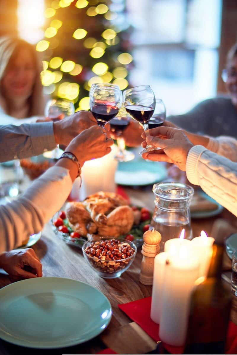 A group of people toasting with red wine glasses over a festive dinner table