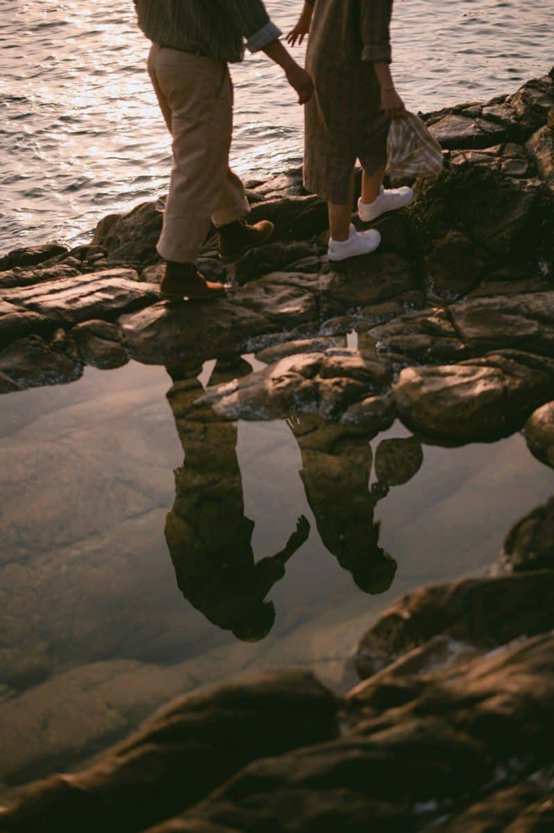 Two people walking on rocky shore with their reflections in a tide pool