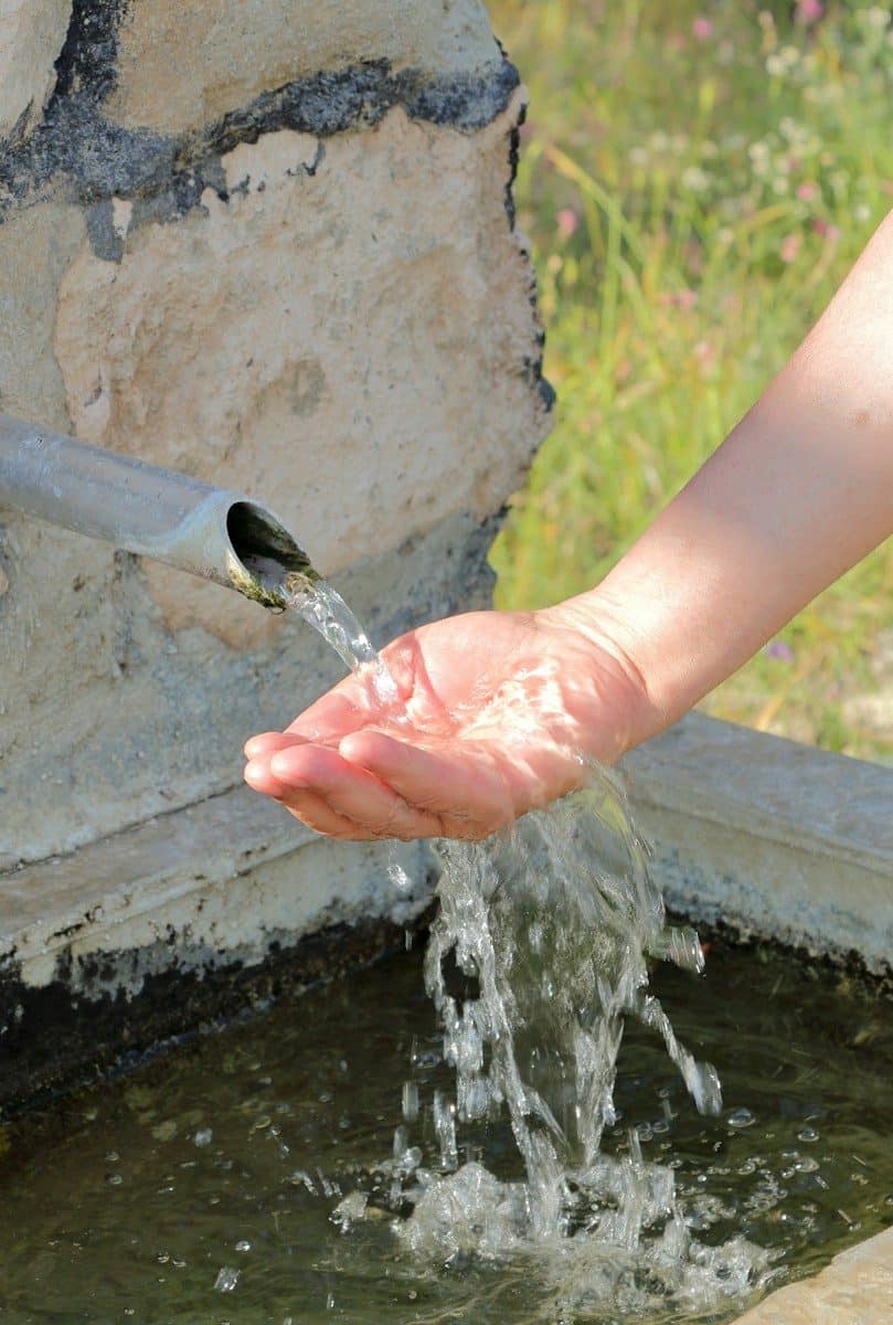 A hand catches fresh water flowing from a stone fountain
