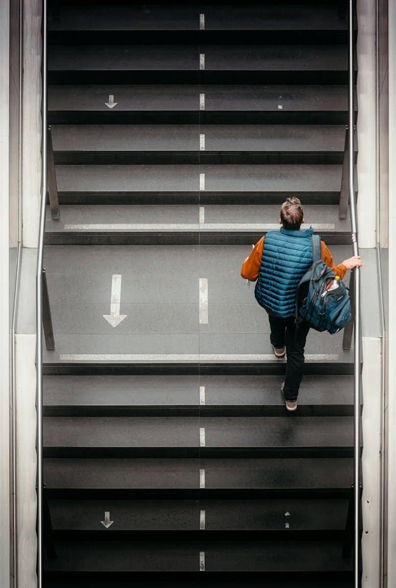 Man with backpack walks up escalator stairs