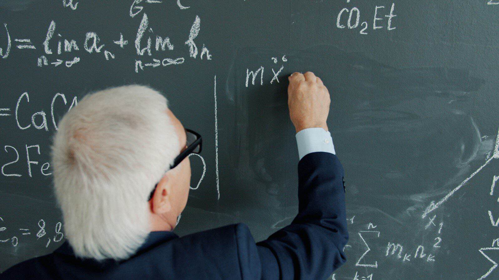Elderly professor writing mathematical equations on a blackboard
