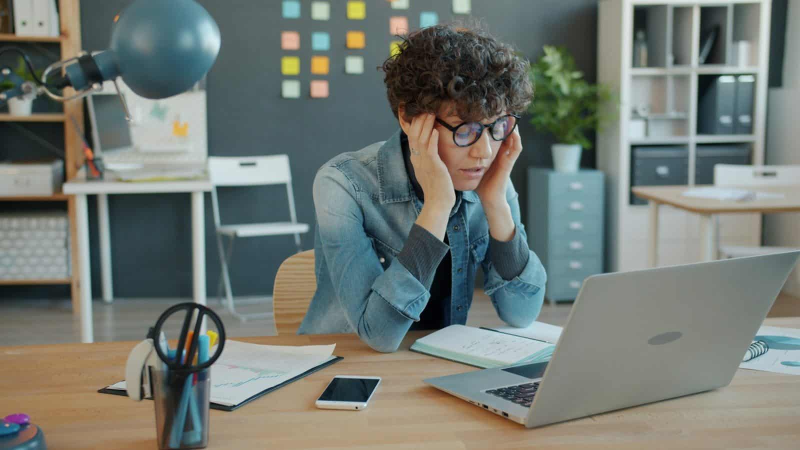 A person looking stressed at a laptop in an office
