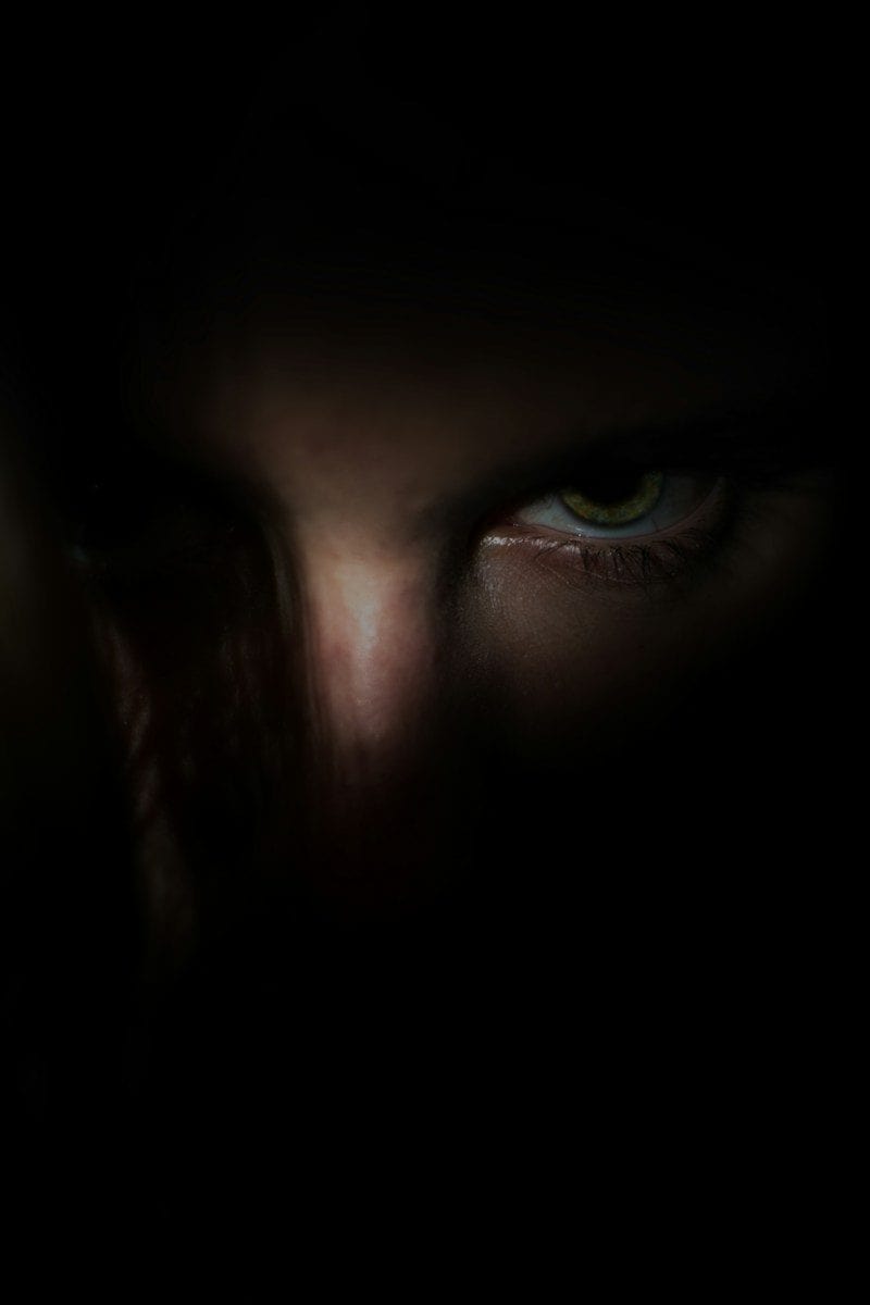 A close-up of a single green eye emerging from deep shadows