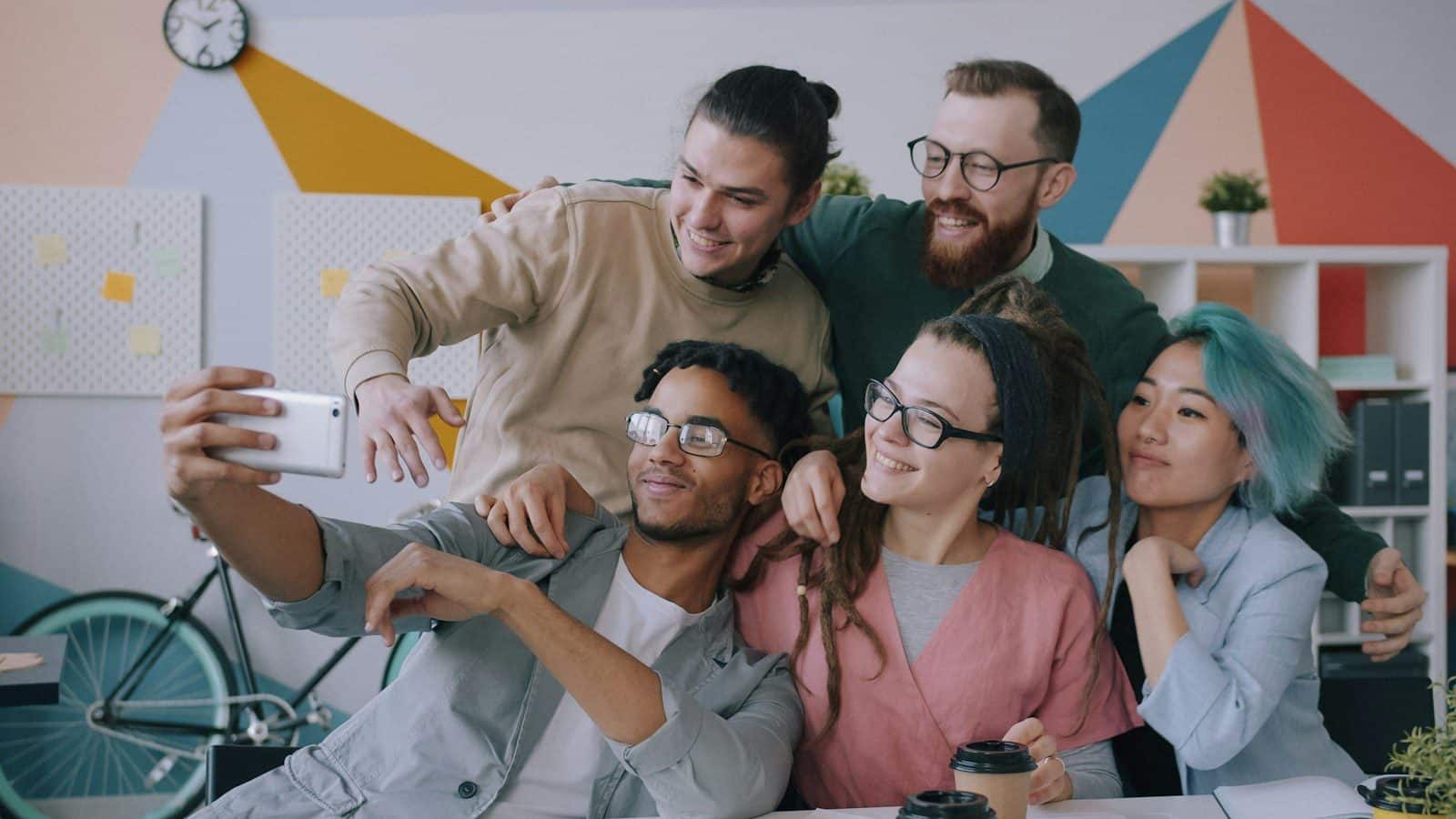 A diverse group of five people taking a selfie in a colorful office workspace