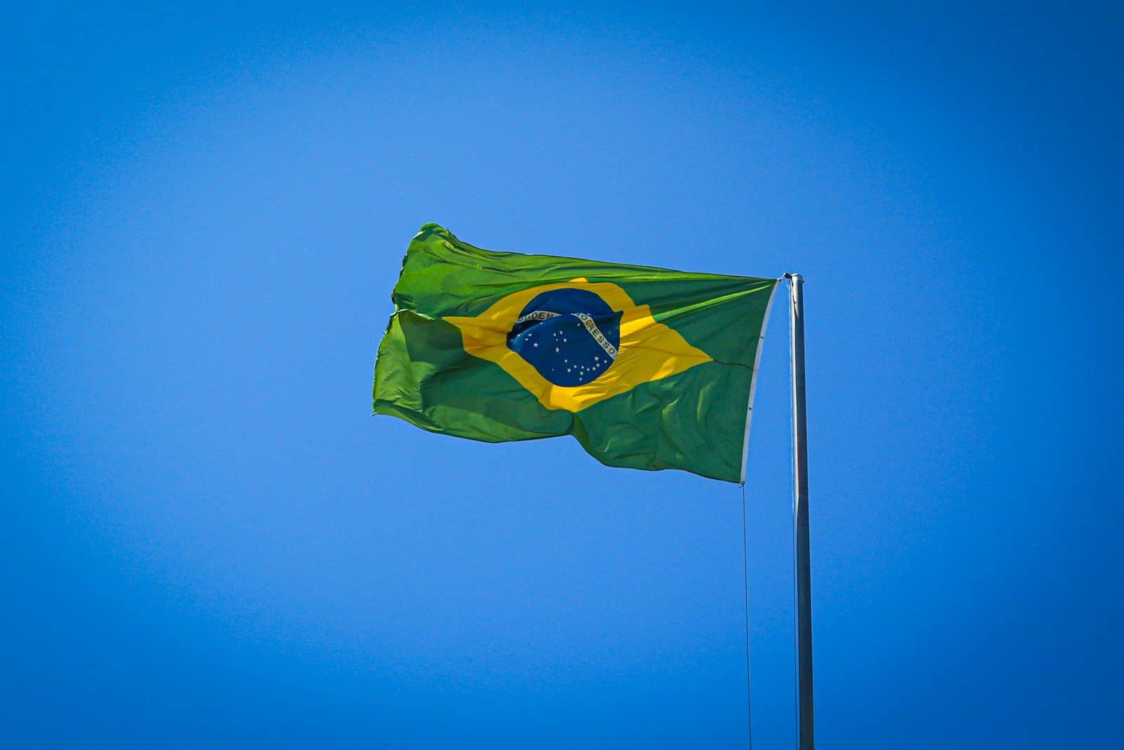 The flag of Brazil waving on a pole against a clear blue sky