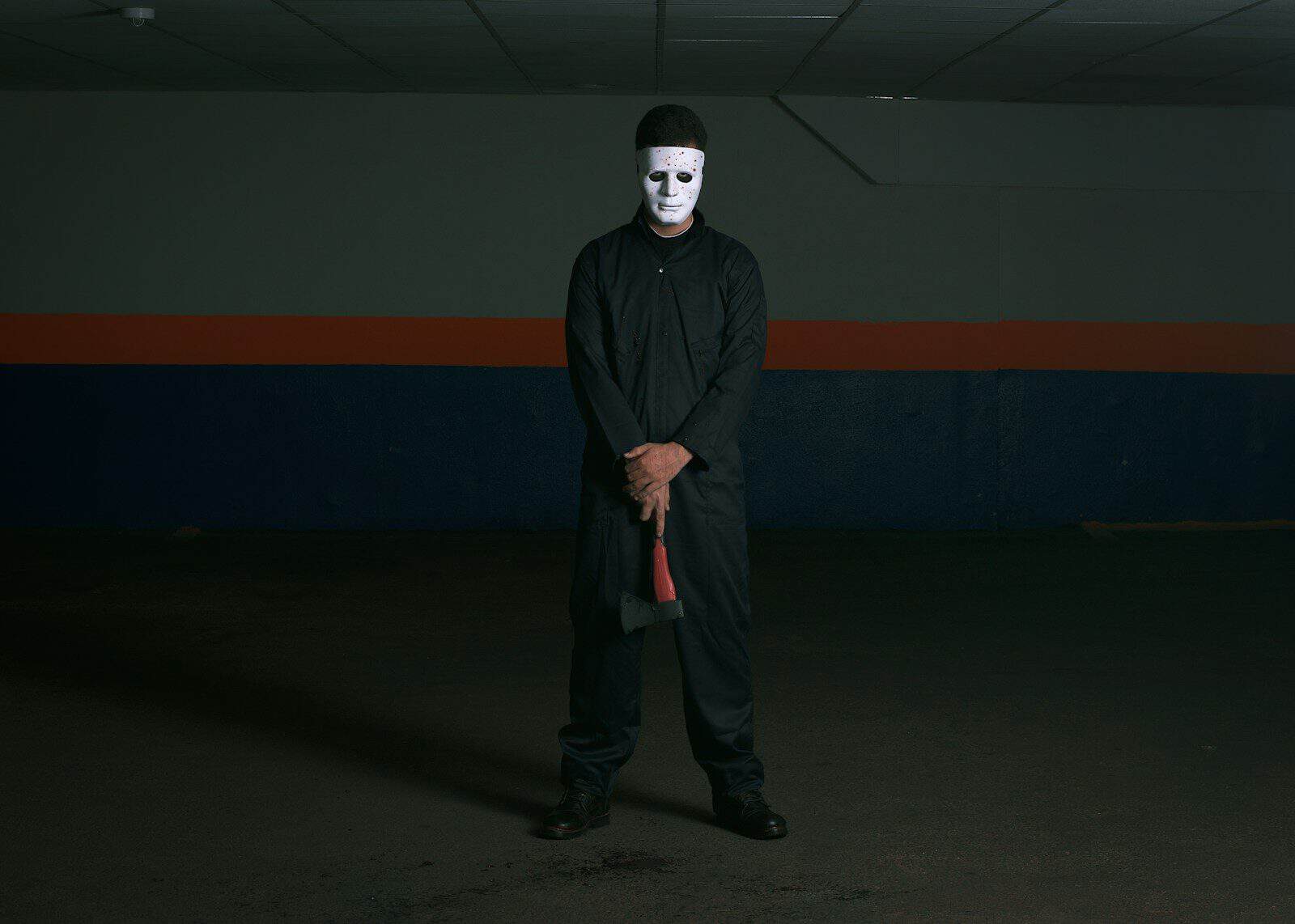 man wearing mask holding axe standing near wall